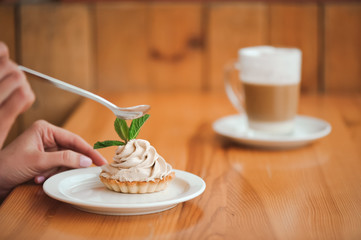 Woman eating a cake of cottage cheese in a ceramic plate with a spoon on a wooden table