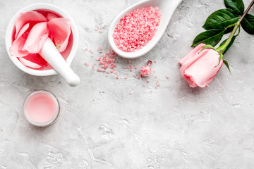 Fototapeta na wymiar Make cosmetics with rose oil. Mortar with rose petals and pestle on grey stone background top view copyspace
