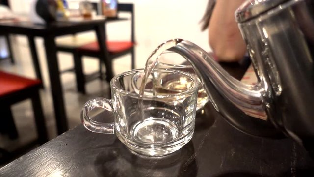 Hot tea from a kettle poured into a glass placed on the table