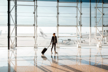 View on the aiport window with woman walking with suitcase at the departure hall of the airport....
