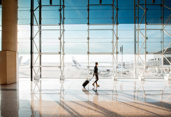 View on the aiport window with woman walking with suitcase at the departure hall of the airport. Wide angle view with copy space