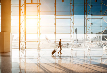 View on the aiport window with woman walking with suitcase at the departure hall during the sunset....
