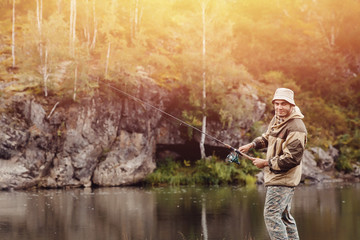 Fishing. The fisherman on a background of rocks throws the fishing rod into the water for catching fish. Concept rest, hobby