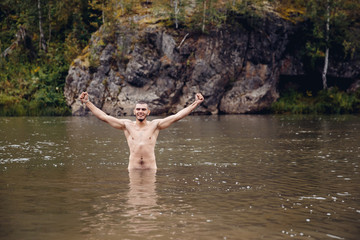 man bathes in a cold river against the background of mountains and rocks