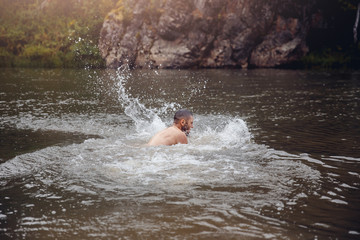 man bathes in a cold river against the background of mountains and rocks