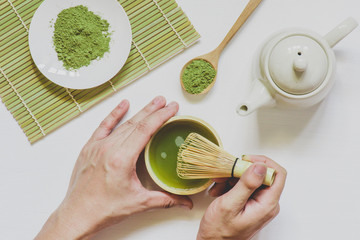 male hands holding cup of green matcha tea on white wooden background