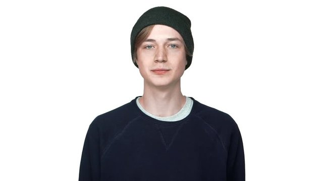 slow motion portrait of calm teenage boy with blue eyes wearing hat posing on camera seriously licking lips isolated over white background closeup. Concept of emotions