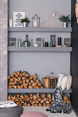 Open dining room interior with firewood, shelves on the grey wall and wooden log wall decoration for warm cozy atmosphere