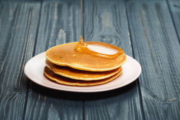Stack of pancakes with honey on wood background