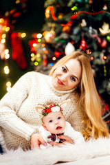Blonde woman in white sweater sits with little girl before a Christmas tree