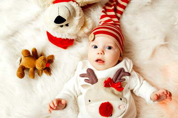 Little baby in sweater with a deer and red hat lies on soft white blanket