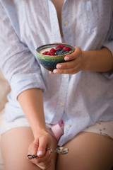 Obraz na płótnie Canvas Woman sitting on a sofa and eating organic yogurt with blueberries and raspberries. Healthy breakfast at home.