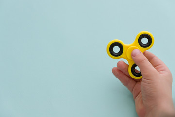 Child's hand spinning a fidget spinner device on light blue background. Top view. Playing with a yellow hand spinner fidget toy - obrazy, fototapety, plakaty