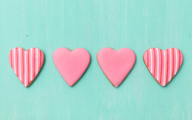 Top view on four pink sugar cookies in heart shape on turquoise wooden background. Valentine's day card.