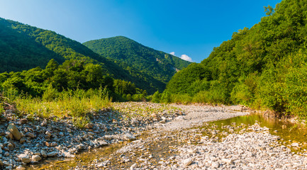 Fototapeta na wymiar Panoramic view of Makopse river flowing in ravine on the background of Tamyurdepe mountain in the light of the setting sun, Sochi, Russia