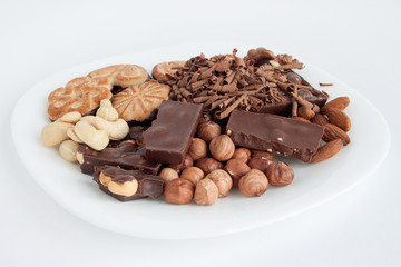 Nuts, chocolate and cookies are lying at the white plate.