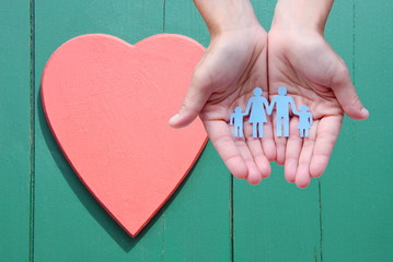 Paper family in hands on wooden background with red heart