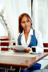 Attractive young woman using digital tablet while drinking coffee in cafe