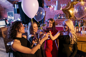 Attractive young female friends celebrating a holiday standing with glasses of wine in trendy bar