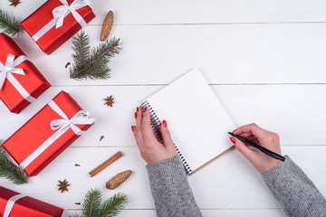 Top view of Christmas background with blank empty diary and girl's hands with pen writing goals on...