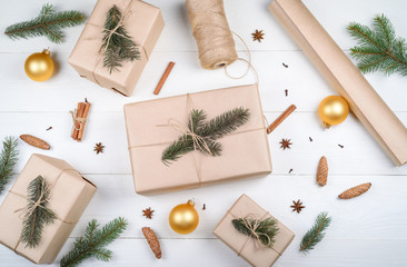 Christmas background with gift boxes wrapped in kraft paper, fir tree branches, golden glass balls, pine cones, cinnamon and star anise on white wooden background. Flat lay, top view
