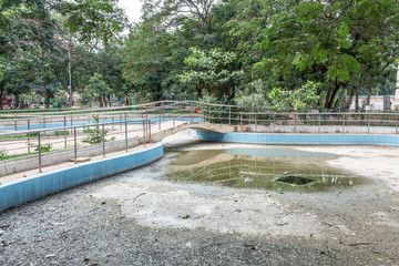 Man made pond with a small foot over bridge with no water in the pond.