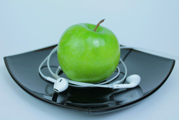 Fresh green apple and headphones on dark plate on white background