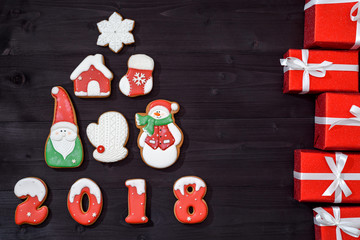 Christmas background with fir tree made from gingerbread cookies and red gifts on wooden background, copy space. New Year 2018 postcard with gingerbread snowman, santa, snowflake, house, mitten, sock