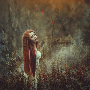 A Beautiful Young Woman With Very Long Red Hair As A Witch Walks Through The Autumn Forest.