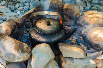 A sooty kettle standing on the campfire surrounded by rocks