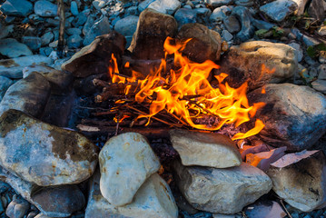 Burning campfire of thin sticks closeup surrounded by rocks 