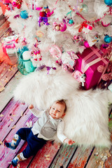 Little baby lies on fluffy carpet before pink present boxes under Christmas tree