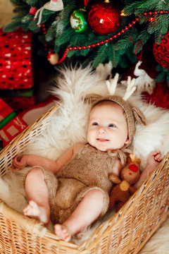 Funny little baby in deer suit lies in a basket before a Christmas tree