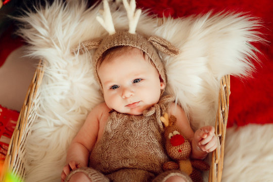 Funny little baby in deer suit lies in a basket before a Christmas tree