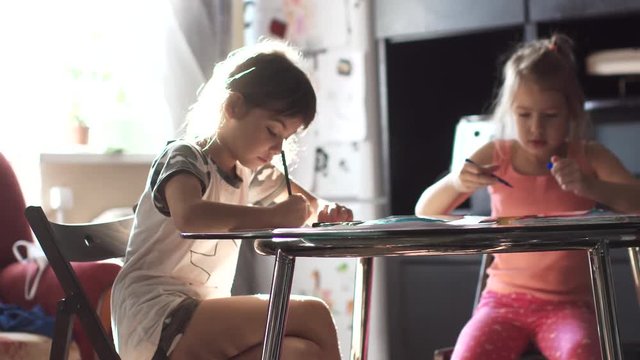 children draw with pencils at home sitting at a table. two little girls sister draw together in the kitchen
