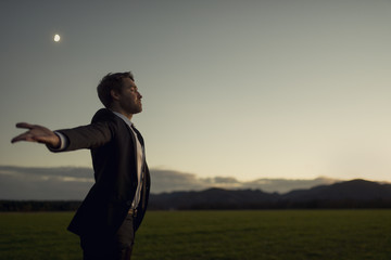 Man in elegant suit standing in nature with his arms spread widely