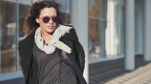 woman in sun glasses a black leather jacket, black jeans posing in front of mirrored windows. Female fashion concept. Outdoor.
