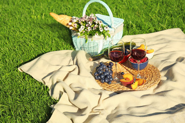 Composition with ripe fruits, wine and picnic basket on blanket outdoors