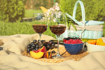 Glasses of wine and fruits for picnic on blanket outdoors