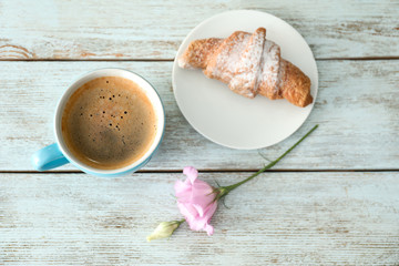 Cup of aromatic morning coffee and croissant on wooden table