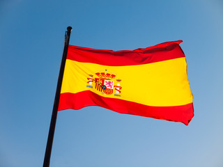 Spanish flag blowing against a blue sky at the mast