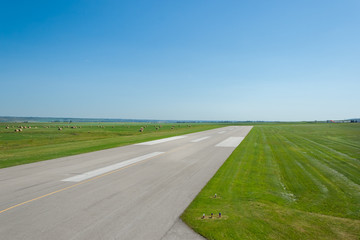 Airport runway with green grass and blue sky in the horizon.