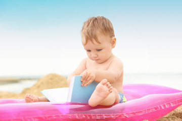 Cute baby boy sitting on inflatable mattress at beach