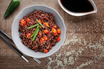 Plate with red rice and vegetables on wooden table