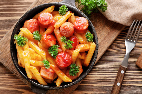 Pasta with sausage in frying pan on wooden background