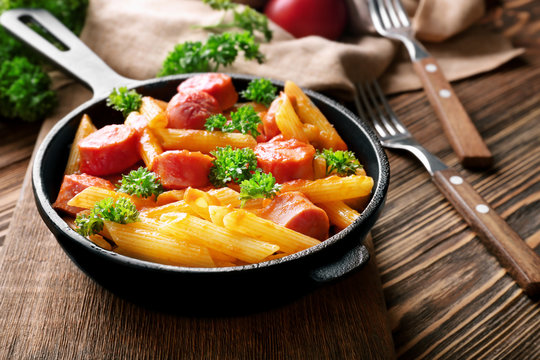 Pasta with sausage in frying pan on wooden background