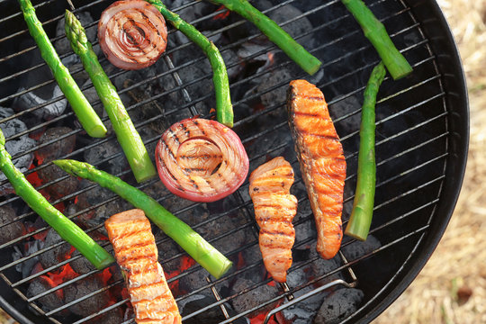 Tasty salmon slices with vegetables on barbecue grill outdoors