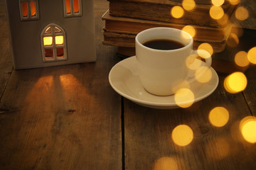 Low key image of house lantern with burning candle and warm light in the windows over old wooden background