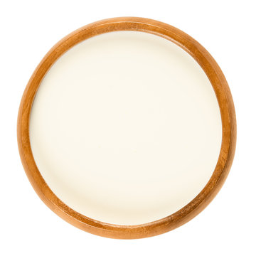 Fresh sweet cream in wooden bowl, a dairy product composed of the higher butterfat layer skimmed from the top of milk before homogenization. Macro food photo close up from above on white background.