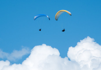 Two paragliders flying in the blue sky against the background of clouds. Paragliding in the sky on a sunny day.